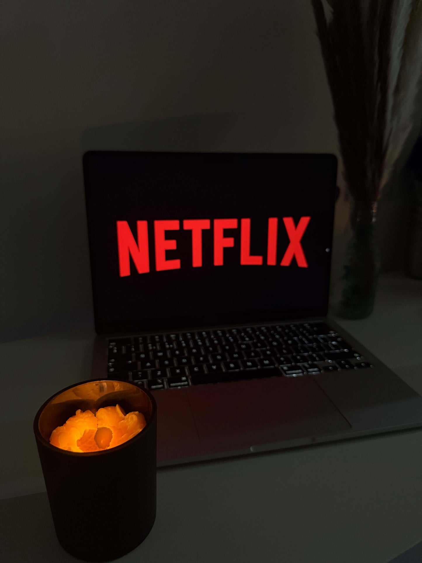 Popcorn theme candle glowing next to a laptop displaying Netflix, perfect for movie date nights.
